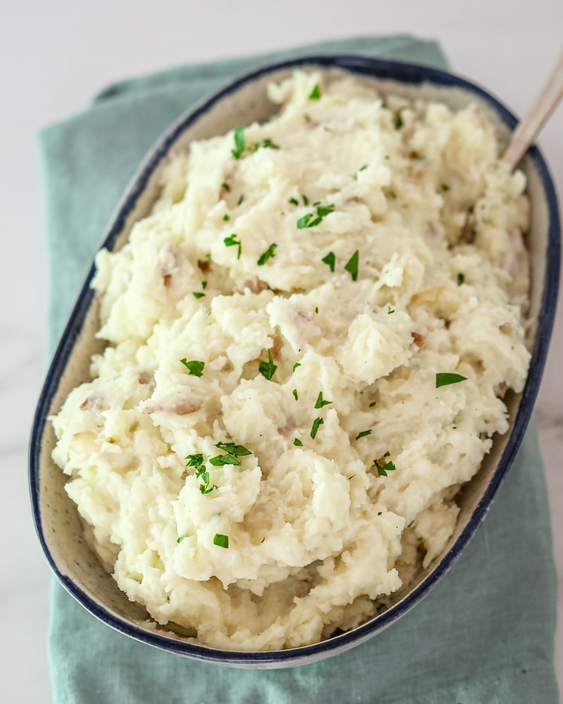 A serving bowl with make-ahead mashed potatoes, garnished with parsley.