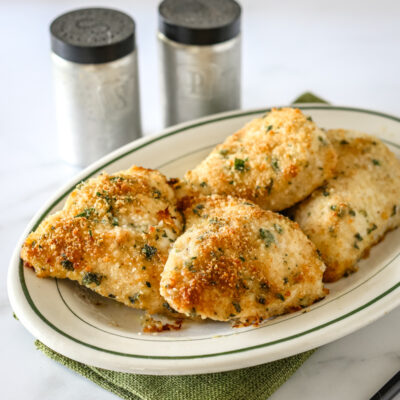 Garlic Parmesan chicken on a serving platter with salt and pepper shakers behind it.
