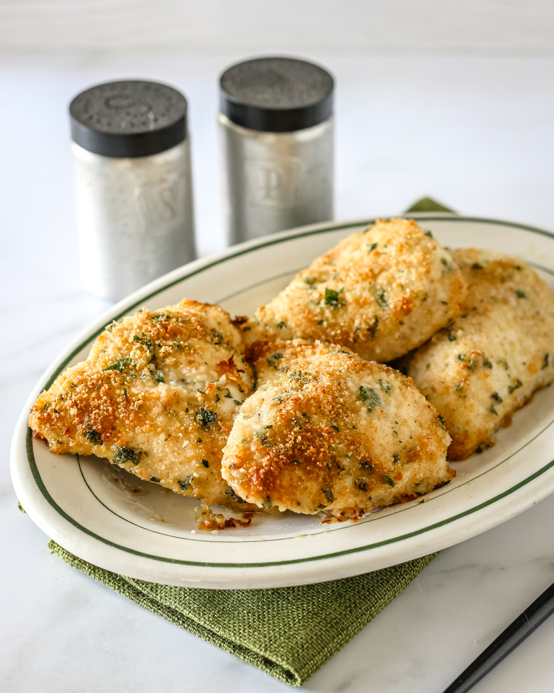 Garlic Parmesan chicken on a serving platter with salt and pepper shakers behind it.