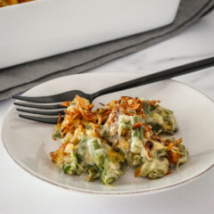 A serving of green bean casserole on a plate with a fork on the side.