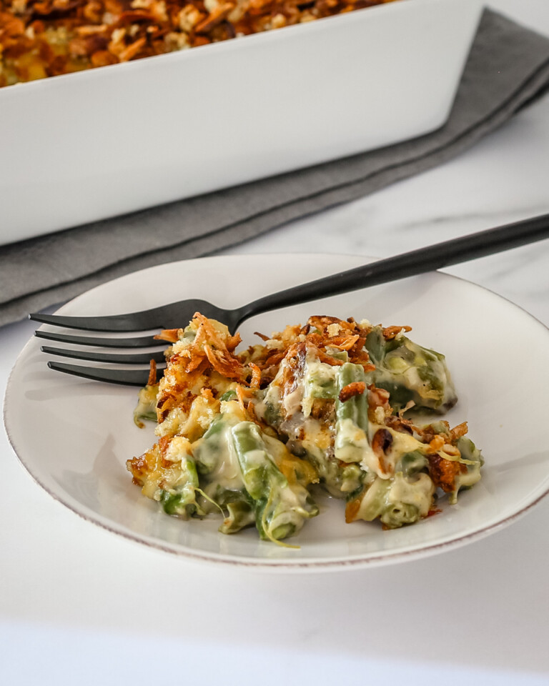 A serving of green bean casserole on a plate with a fork on the side.