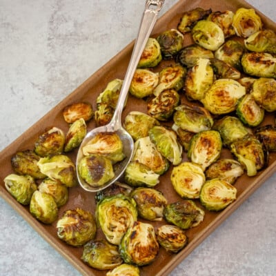 A serving platter with roasted brussels sprouts and serving spoon.