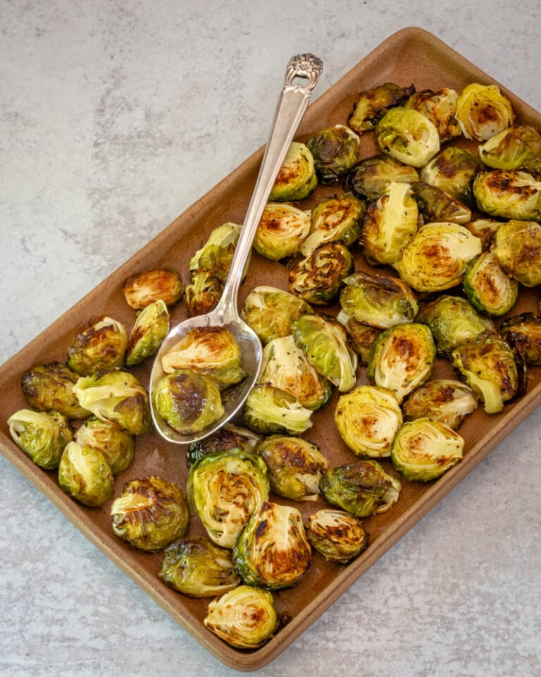 A serving platter with roasted brussels sprouts and serving spoon.