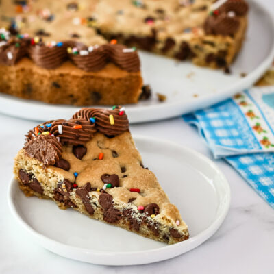 A slice of chocolate chip cookie cake with chocolate frosting and sprinkles.