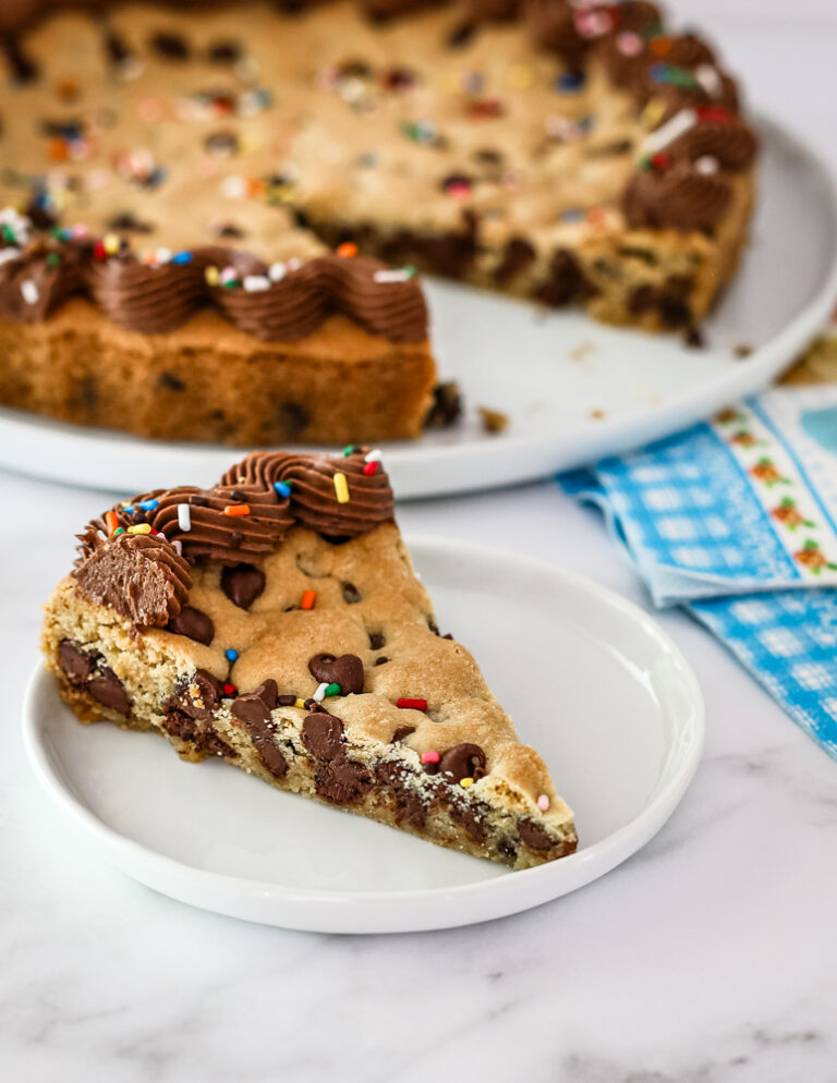 A slice of chocolate chip cookie cake with chocolate frosting and sprinkles.