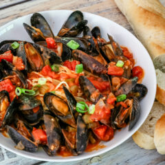 A bowl of mussels with Creole sauce, linguine, and a baguette on the side.