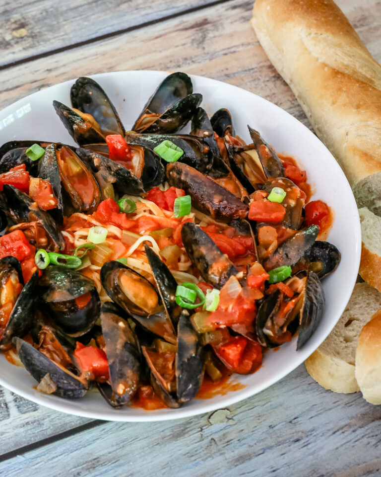 A bowl of mussels with Creole sauce, linguine, and a baguette on the side.