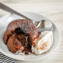 A chocolate fondant, also known as molten lava cake, on a plate with freshly whipped cream and a light dusting of cocoa and powdered sugar.