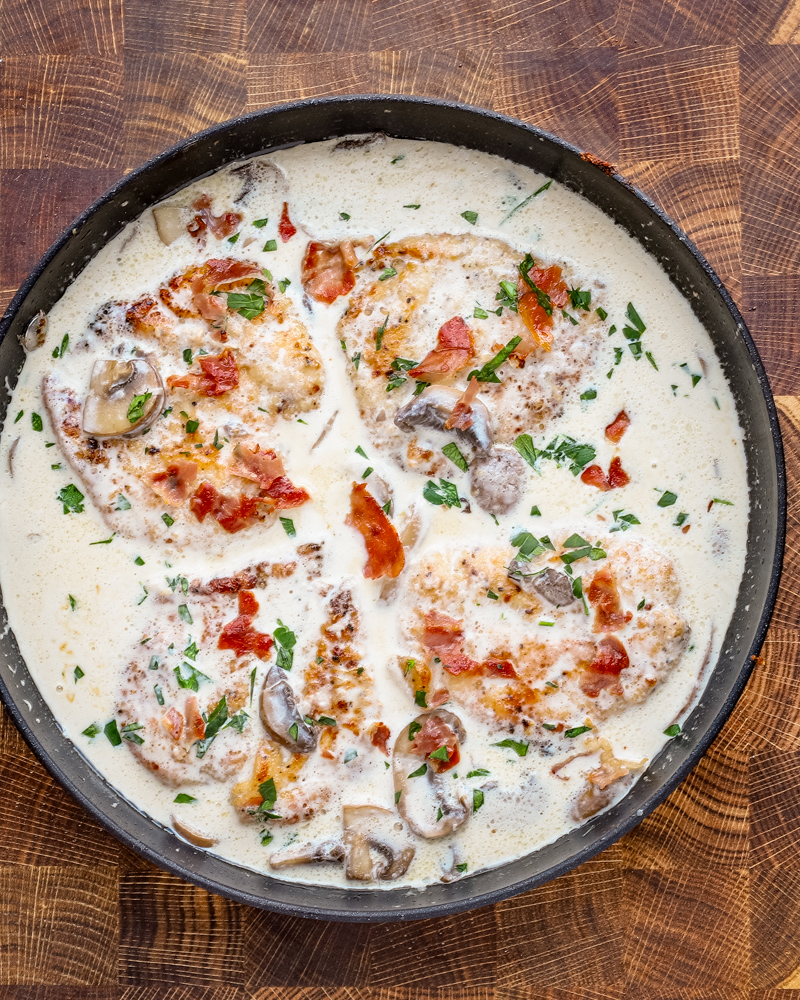 Cooked chicken breasts in a creamy wine sauce garnished with parsley and crispy prosciutto.