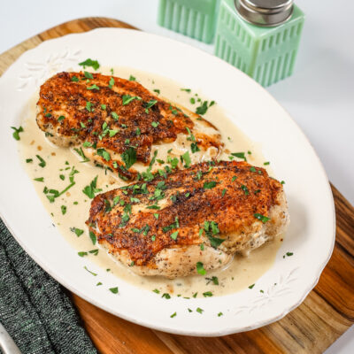 Dijon chicken with a creamy sauce and herb garnish on a white plate.