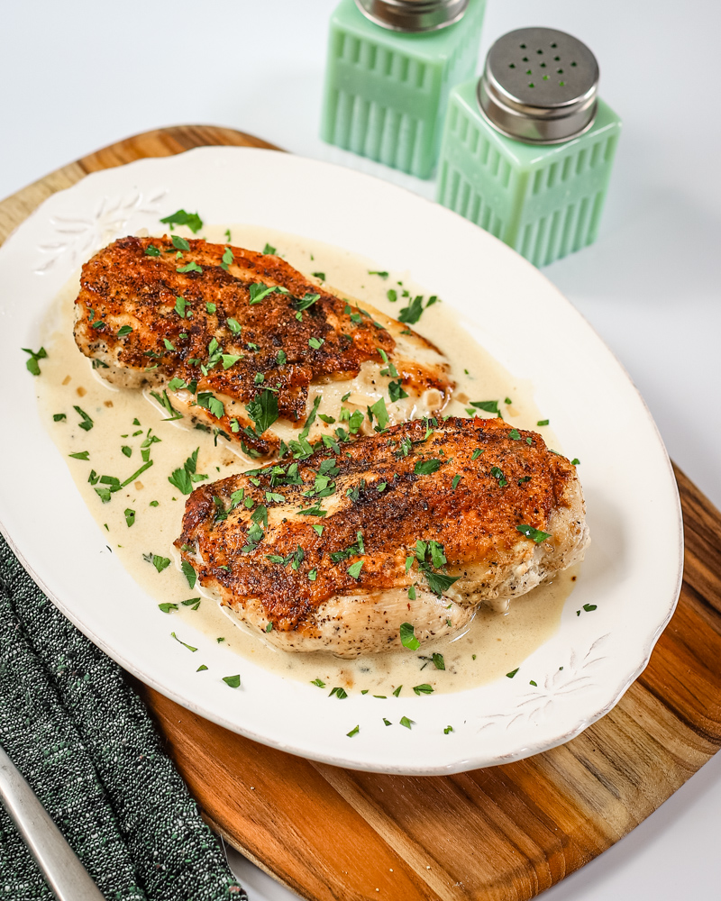 Dijon chicken with a creamy sauce and herb garnish on a white plate.