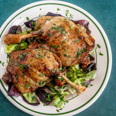 Duck confit on a plate with spring greens and parsley.