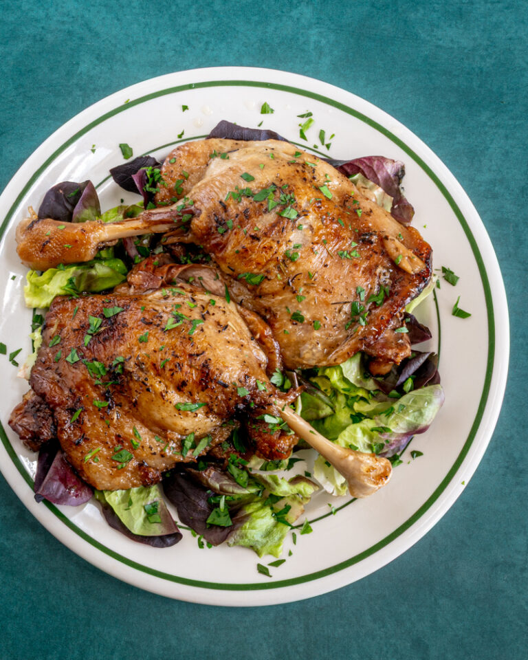 Duck confit on a plate with spring greens and parsley.