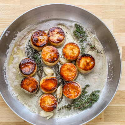 Butter, smashed garlic, and thyme are added to the skillet to flavor the fondant potatoes.