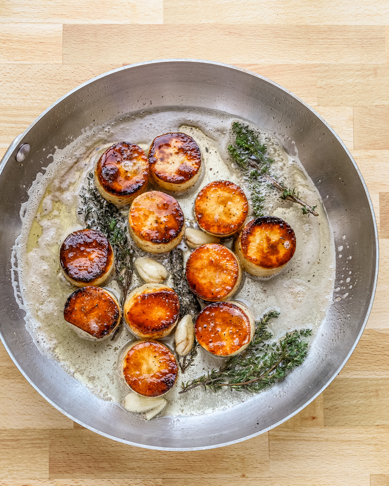 Butter, smashed garlic, and thyme are added to the skillet to flavor the fondant potatoes.