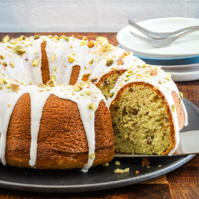 A slice being taken out of an iced pistachio pudding cake.