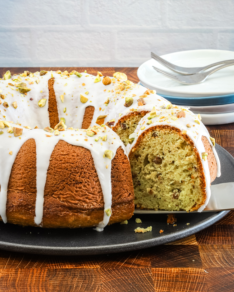 A slice being taken out of an iced pistachio pudding cake.