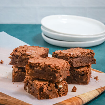 Brownies on a wax paper-lined board with plates in the background.