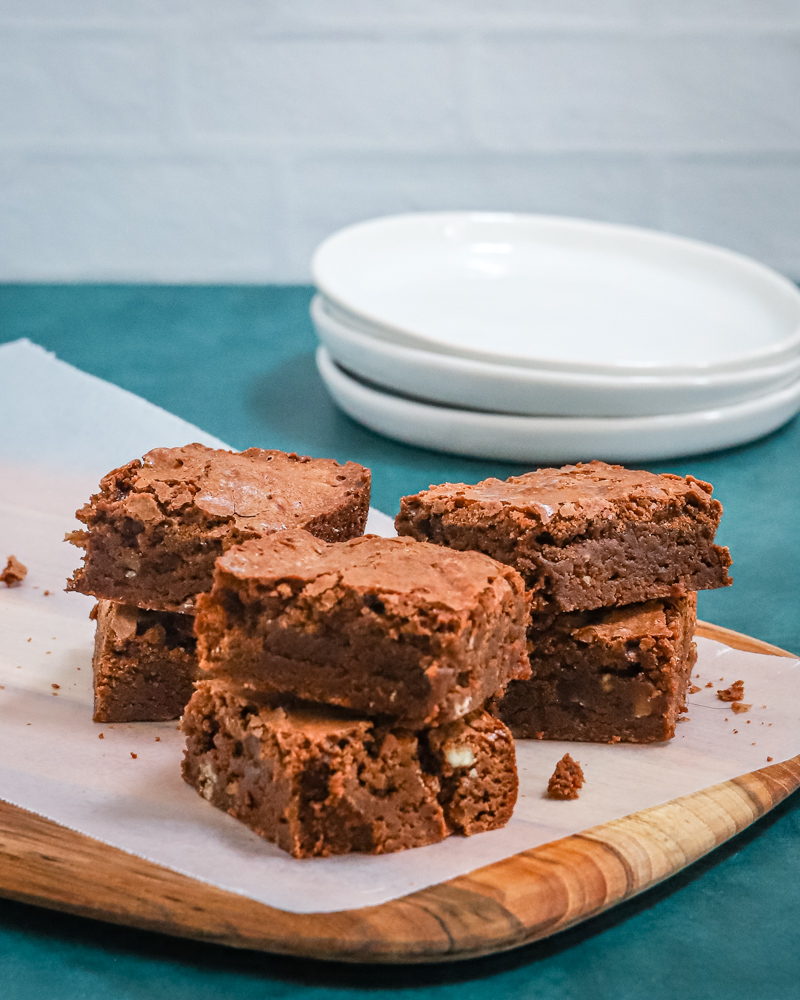 Brownies on a wax paper-lined board with plates in the background.