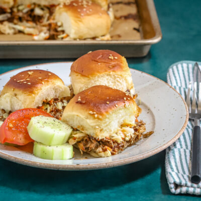 A plate of pulled pork sliders with cucumbers and tomatoes on the side.