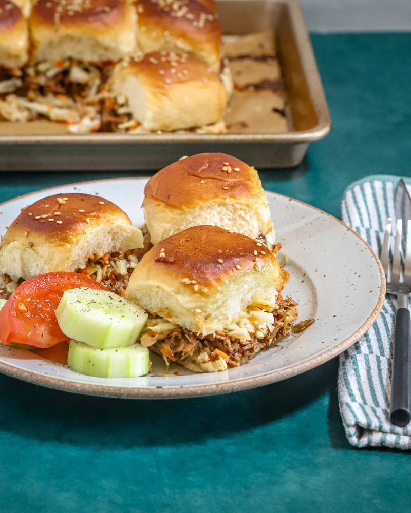 A plate of pulled pork sliders with cucumbers and tomatoes on the side.