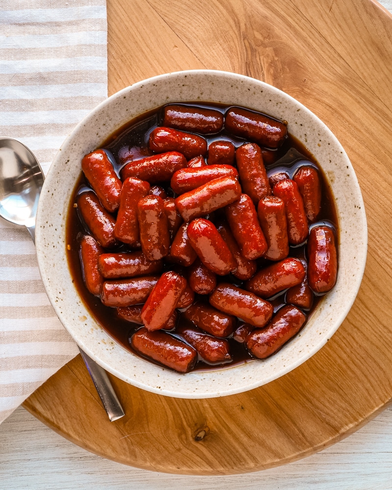Sweet glazed little smokies with rich sauce in a white bowl.