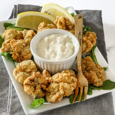 A ramekin with homemade tartar sauce shown with fried oysters.