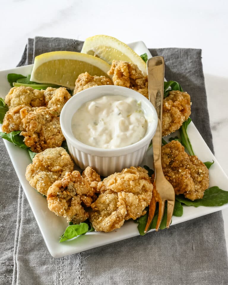 A ramekin with homemade tartar sauce shown with fried oysters.