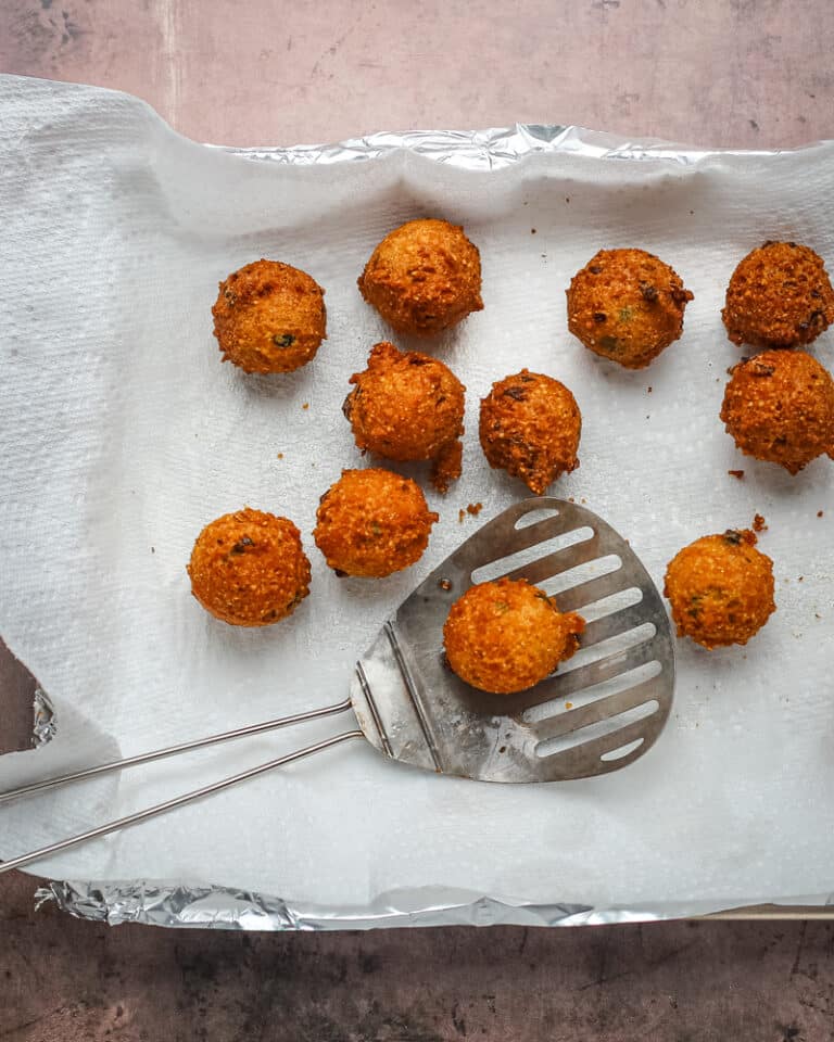 Freshly fried hush puppies from the fryer, draining on paper towels.