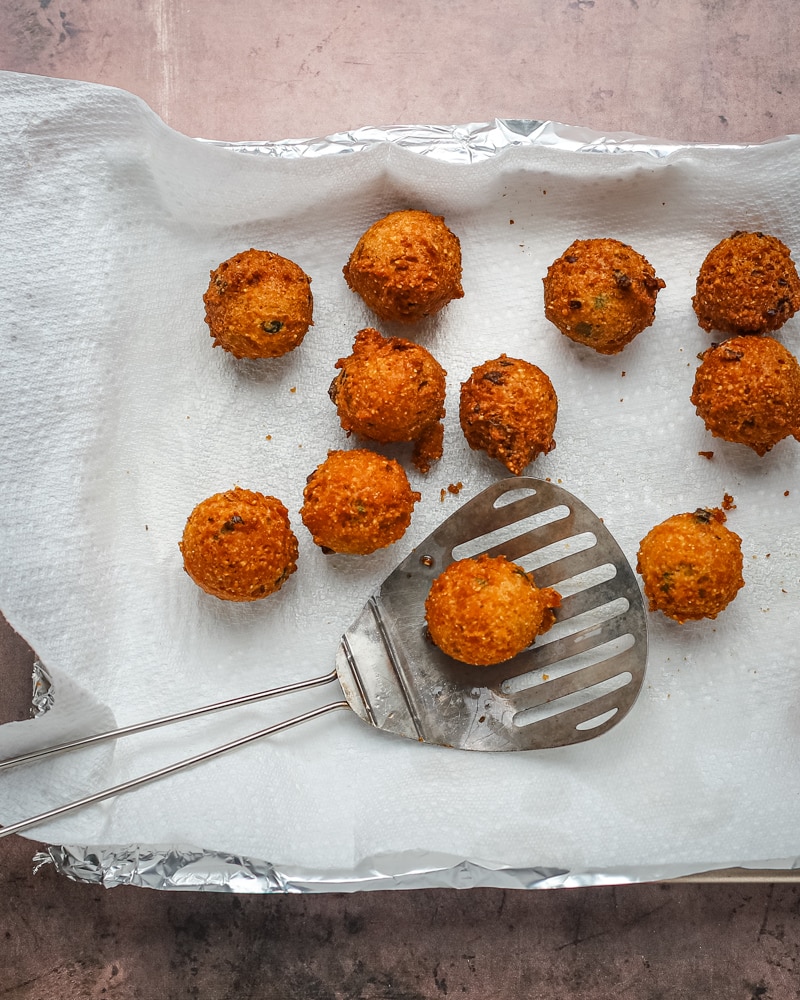 Freshly fried hush puppies from the fryer, draining on paper towels.