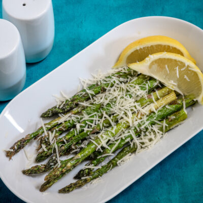 Air fryer asparagus with Parmesan cheese and lemon wedges, on a white tray.