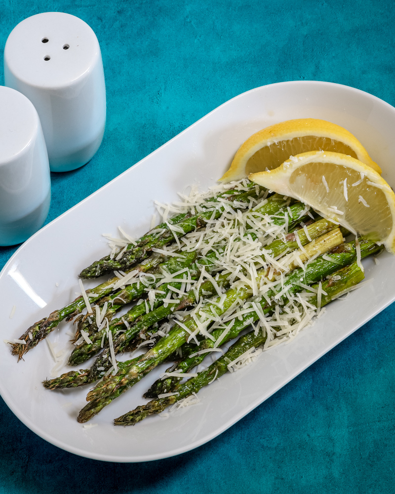 Air fryer asparagus with Parmesan cheese and lemon wedges, on a white tray.