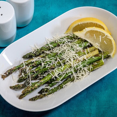 Air-fried asparagus with grated cheese and lemon wedges on white plate.