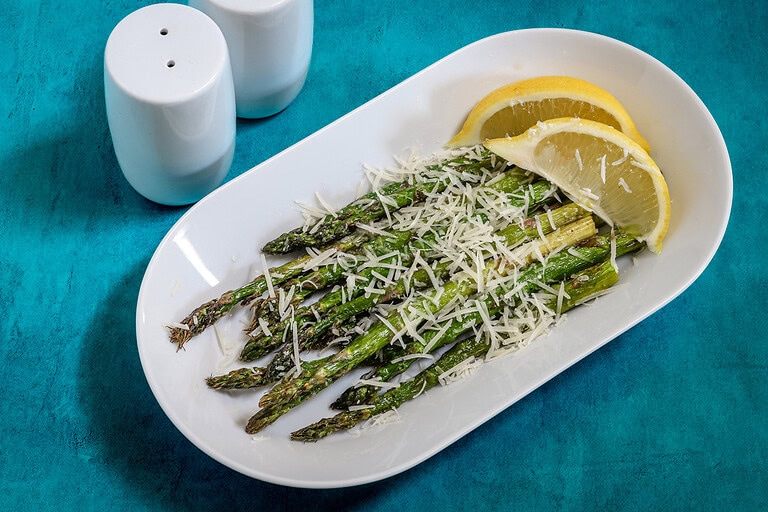 Air-fried asparagus with grated cheese and lemon wedges on white plate.