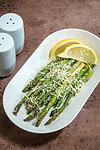 Air-fried asparagus topped with cheese and lemon wedges on a white plate.