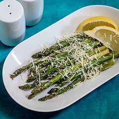 Air fryer asparagus topped with cheese and lemon slices on white plate.