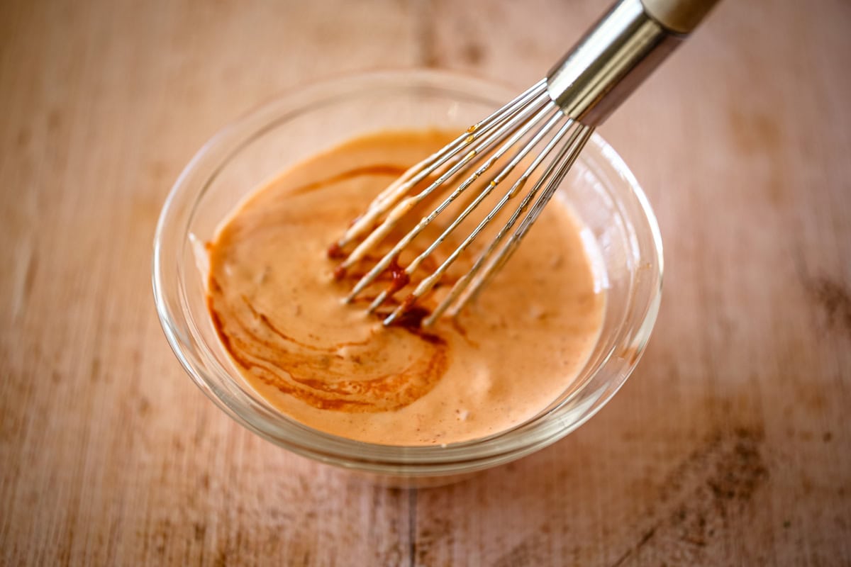 Preparing the Sriracha mayo in a small bowl with a whisk.