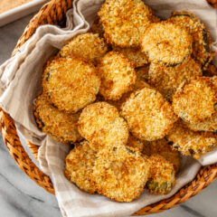 Air fryer pickle slices in a basket with Sriracha mayo on the side.