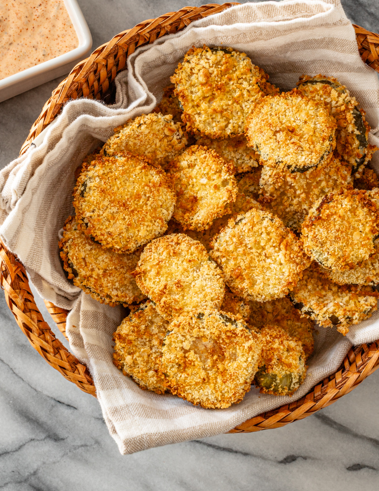 Air fryer pickle slices in a basket with Sriracha mayo on the side.