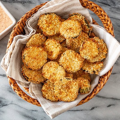 Air fryer pickle slices in a basket with Sriracha mayo on the side.