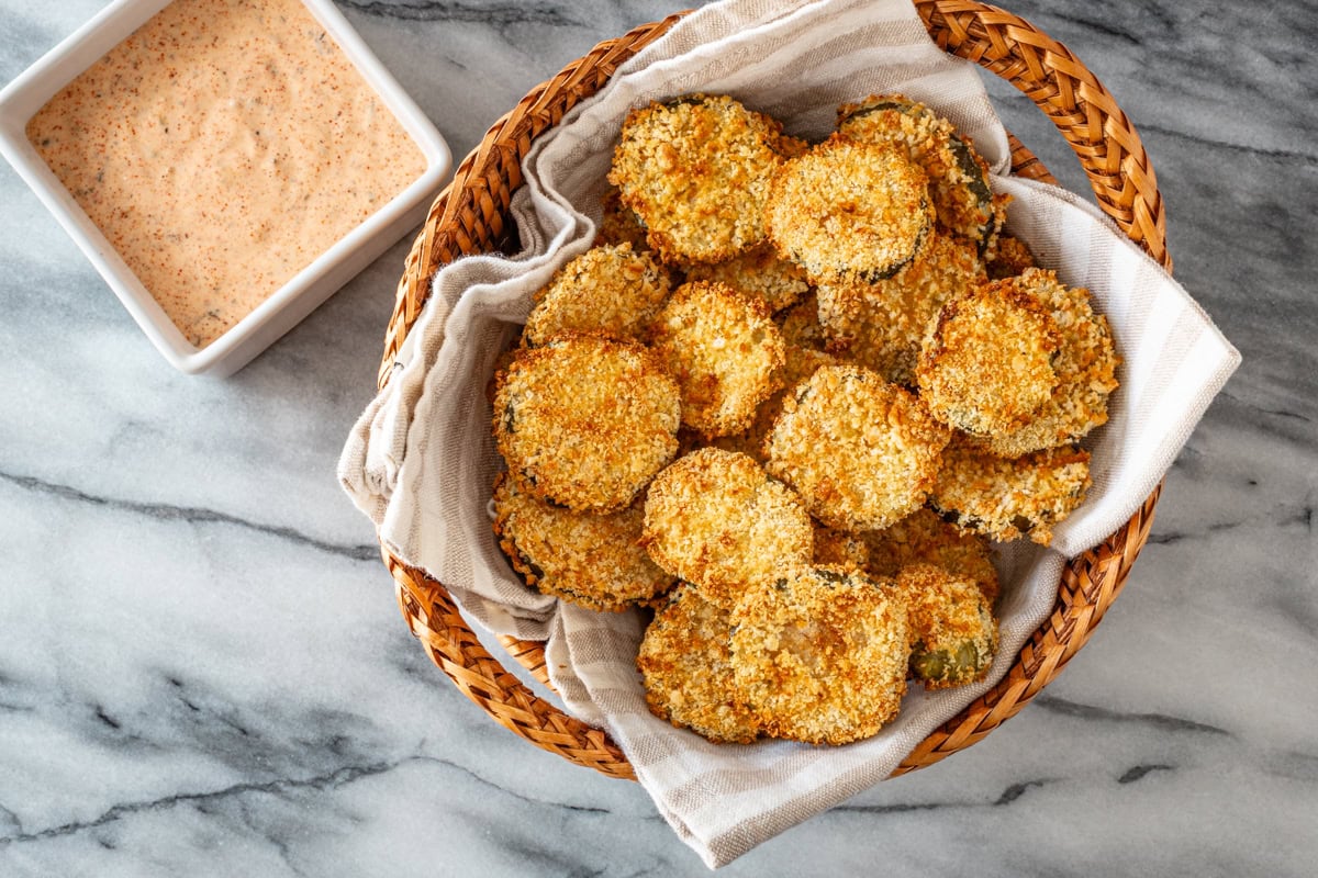 Air fryer pickle slices in a basket with Sriracha mayo on the side.