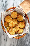 Air fryer pickle slices in a basket with Sriracha mayo on the side.