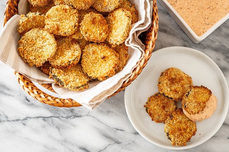 Air fryer pickle slices in a basket with Sriracha mayo on the side.
