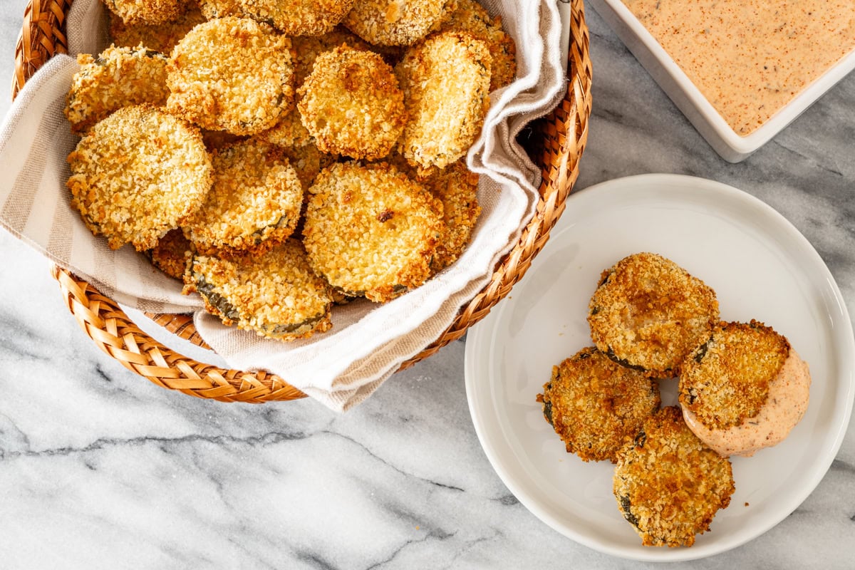 Air fryer pickle slices in a basket with Sriracha mayo on the side.