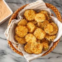 Air fryer pickle slices in a basket with Sriracha mayo on the side.