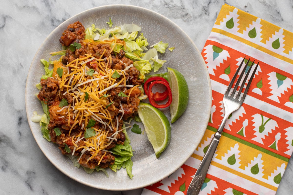 beef and bean taco casserole shown in a pan with melted cheese topping and cilantro leaves