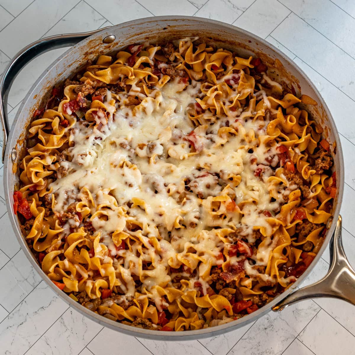 Beef and noodles with a cheese topping, in a skillet.