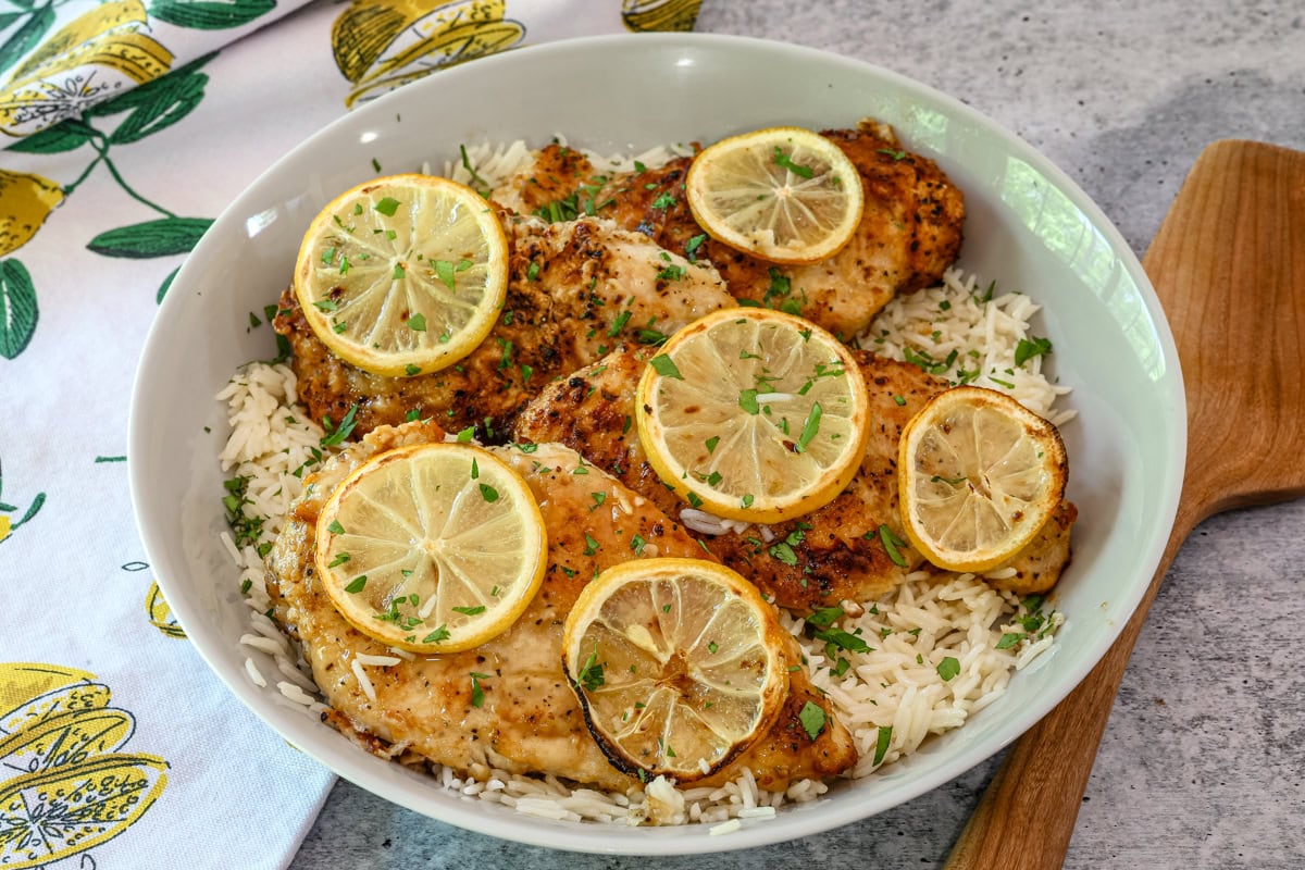A serving bowl of lemon pepper chicken on rice with charred lemon slices.