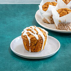 Pumpkin muffins with a drizzled glaze with more muffins in the background.