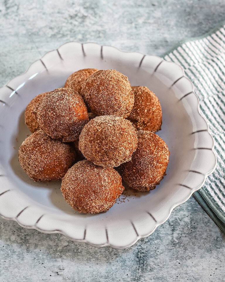 Cinnamon sugar coated pumpkin fritters stacked on a plate with a cloth on the side.